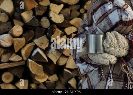 Donna in plaid tiene la tazza di metallo contro lo sfondo di legna da ardere Foto Stock