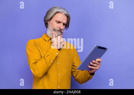 Ritratto di attraente uomo focalizzato grigio-capelli utilizzando tablet pensiero isolato su sfondo viola brillante viola Foto Stock