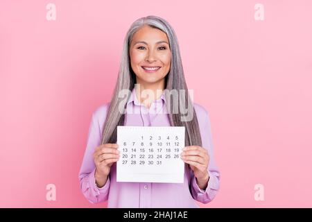 Ritratto di attraente allegro grigio-capelli donna tenuta in mani calendario isolato su rosa pastello sfondo colore Foto Stock