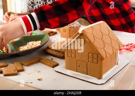 I bambini che assemblano e decorano una casa di pan di zenzero al tempo di Natale. Tradizione di famiglia di Natale, artigianato di Natale. Foto Stock