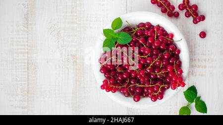 Bacche fresche e succose crude di ribes rosso e foglie di menta in piatto bianco. Messa a fuoco selettiva. Vista dall'alto Foto Stock