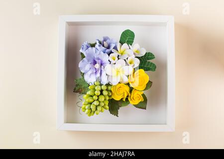 Bouquet di piccoli fiori luminosi in argilla polimerica in cornice su beige chiaro Foto Stock