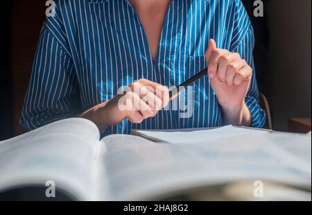 Le donne hanno le mani con la penna in primo piano studiando e scrivendo con un sacco di libri. Foto Stock