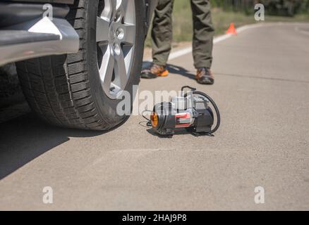 Pompa pneumatico portatile per gonfiare la ruota dell'auto su strada. Compressore pneumatico con manometro. Foto Stock