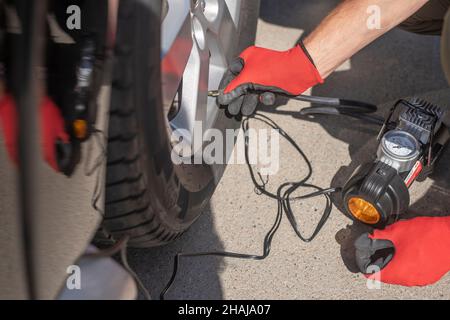 Gonfiaggio della ruota della vettura con pompa pneumatici. Gonfiagomme in mani maschili. Foto Stock