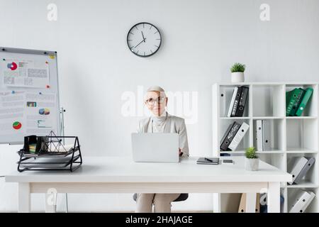 donna d'affari con capelli grigi seduti alla scrivania con computer portatile Foto Stock