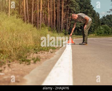Uomo che mette il triangolo rosso cartello di attenzione sul lato della strada in natura. Foto Stock