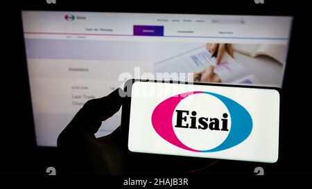 Persona che tiene uno smartphone con il logo della società farmaceutica giapponese Eisai Co. Ltd. Sullo schermo di fronte al sito web. Mettere a fuoco sul display del telefono. Foto Stock