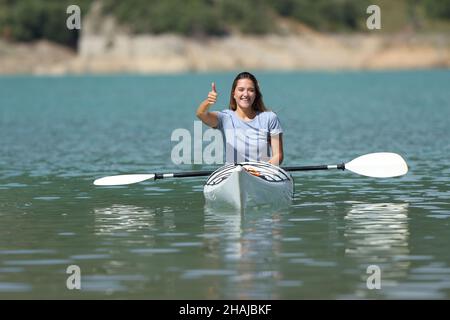 Vista frontale ritratto di una donna felice gesturando pollice in un kayak in un lago in vacanza estiva Foto Stock