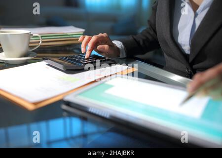 Contabilità a mano di una donna d'affari con calcolatrice e tablet su una scrivania di notte in ufficio Foto Stock