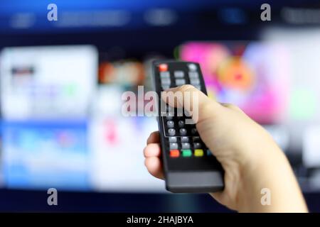 Mano femmina con telecomando sullo sfondo dello schermo della Smart TV. Donna che sceglie i servizi di streaming, guardando i film Foto Stock