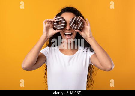 Felice Lady Latina che copre gli occhi con le ciambelle allo Studio Foto Stock