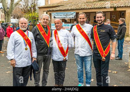 Cinque uomini che indossano le fasce rosse e le medaglie di una confraternita gastronomica posano sorridenti davanti alla sala del mercato all'apertura della stagione del mercato dei tartufi di Aups, dipartimento di Var, Francia, tradizionalmente tenuto il primo giovedì di dicembre Foto Stock