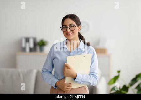 Ritratto di psicologa felice medio-orientale sorridendo a macchina fotografica durante la sessione di terapia, lavorando in clinica Foto Stock