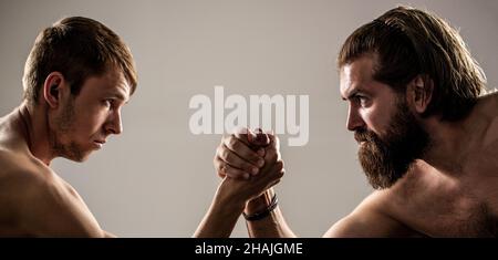 Armi che lottano mano sottile, grande braccio forte in studio. Due mani di uomo hanno stretto il braccio wrestling, forte e debole, corrispondenza disuguale. Uomo pesantemente muscled bearded Foto Stock
