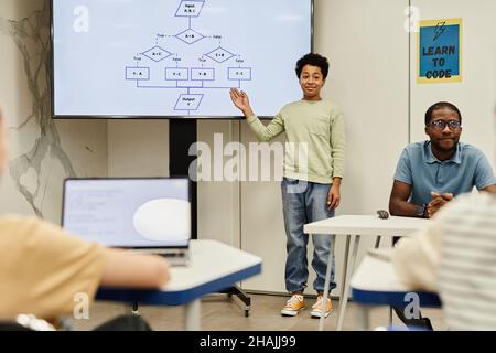 Ritratto a tutta lunghezza di ragazzo sorridente che dà la presentazione in classe di codifica per i bambini, spazio di copia Foto Stock