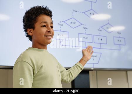 Ritratto di ragazzo sorridente che dà la presentazione in classe di codifica per i bambini e puntando a schermo digitale, spazio copia Foto Stock