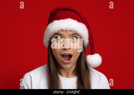 Offerta incredibile. Ritratto di donna scioccata indossando Santa Hat guardando la fotocamera Foto Stock