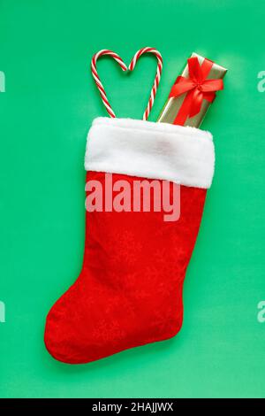Calza di Natale con piccola scatola regalo e caramelle a forma di cuore su sfondo verde con spazio per la copia del testo. Composizione piatta di vacanza de Foto Stock