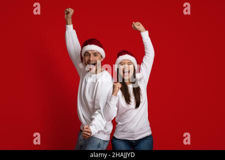 Festa di Natale. La coppia overjoyed in cappelli di Santa che celebra il successo con i fists sollevati Foto Stock