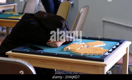 Una ragazza che è molto stanca dopo aver giocato a lungo mahjong. La ragazza con lunghi capelli neri si stese per riposare sul tavolo mahjong. Tradizionale asiatico Foto Stock