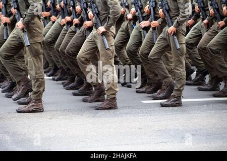 Messa a fuoco selettiva. Sfocatura del movimento. Scarpe militari moderne sui soldati. Un soldato in uniforme sta marciando nella sfilata. Persone nella folla. Stivali sul piede. Foto Stock