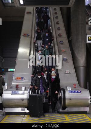 Pendolari su una scala mobile alla stazione della metropolitana di Canary Wharf alle 16:51 nell'ora di punta della sera, dove sono state introdotte nuove restrizioni per rallentare la diffusione della variante Omicron del coronavirus. Data foto: Lunedì 13 dicembre 2021. Foto Stock