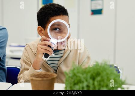 Ritratto di ragazzino adolescente che gioca con lente di ingrandimento a scuola Foto Stock