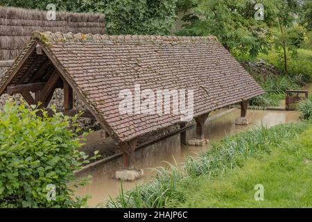 Lavare casa con tetto piastrellato vicino ad un ruscello con acqua in piedi sotto Foto Stock