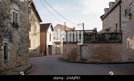 Guardando lungo una strada in un piccolo villaggio francese con edifici tradizionali e ornati pali in pietra intagliata Foto Stock