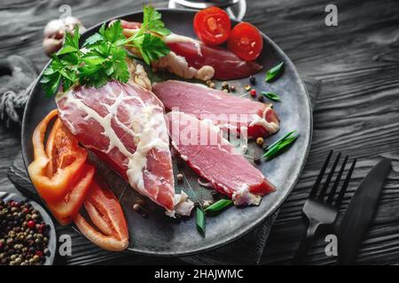 grande pezzo di carne secca in una sottile maglia di grasso interno. Un pezzo di carne fresca affumicata giace sulle foglie di spinaci. Filetto di carne di cervo naturale con Foto Stock