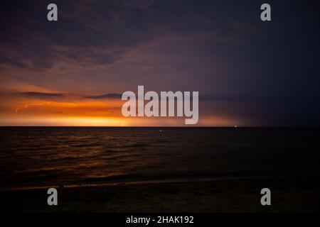 I fulmini illuminano il cielo di notte in mare Foto Stock