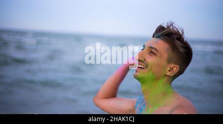 Un ragazzo giovane getta polvere di colore sullo sfondo del mare Foto Stock