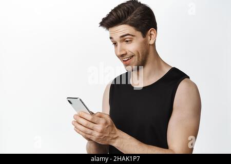 Immagine dell'uomo caucasico adulto che guarda il suo schermo del telefono con il volto sorpreso. Giovane ragazzo entusiasta che sta fissando l'applicazione per smartphone, sfondo bianco Foto Stock