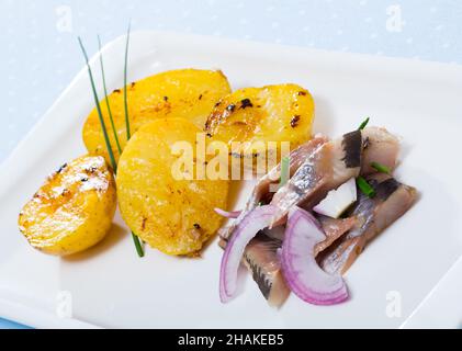 Fette di aringa leggermente curata con patate fritte e cipolle servite sul piatto a tavola Foto Stock