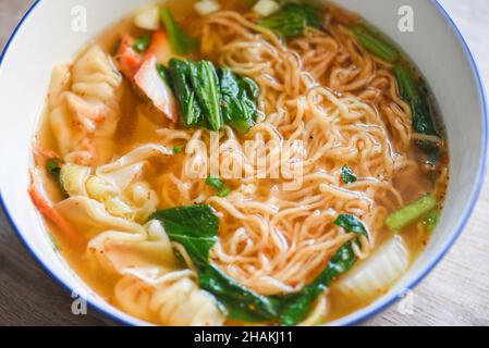 spaghetti per zuppa, spaghetti gialli di maiale wonton con gnocchi di maiale arrostiti rossi e verdure cinesi al brace in ciotola per zuppa su tavolo di legno, vista dall'alto Foto Stock