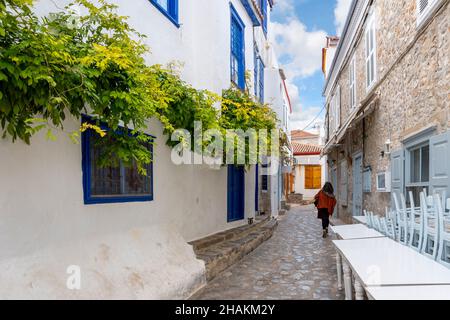 Una donna cammina attraverso un vicolo colorato e stretto sull'isola di Idra, una delle isole Saroniche della Grecia Meridionale. Foto Stock
