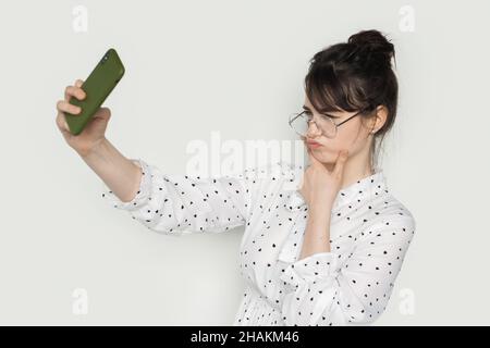 Vista laterale di uno studente che fa un viso d'anatra e che prende un autoritratto con il suo smartphone. Foto Stock