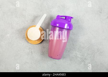 Agitatore e misurino di polvere proteica su fondo di calcestruzzo grigio. Disposizione piatta. PRIMO PIANO Foto Stock