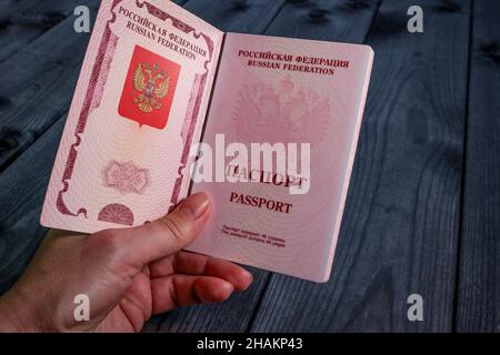 Passaporto internazionale della Federazione Russa in una mano femminile su sfondo di legno sfocato. Concetto di viaggio. Foto Stock