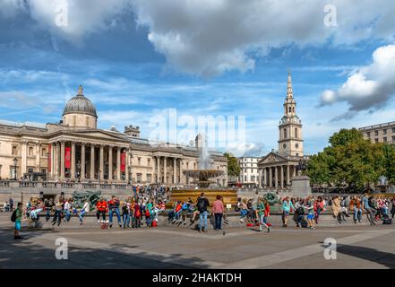 Turisti a Trafalgar Square in un pomeriggio soleggiato in autunno. La Galleria Nazionale e la chiesa di San Martino-in-the-Fields sono sullo sfondo. Foto Stock