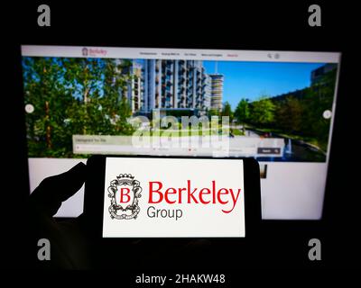 Persona che tiene smartphone con il logo della società britannica The Berkeley Group Holdings plc sullo schermo di fronte al sito web. Mettere a fuoco sul display del telefono. Foto Stock