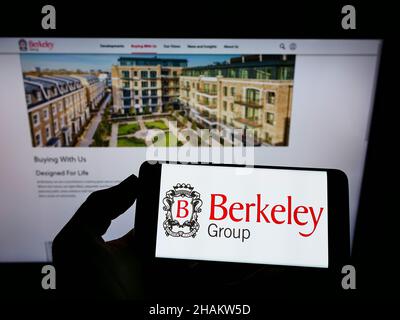 Persona che detiene il cellulare con il logo della società britannica The Berkeley Group Holdings plc sullo schermo di fronte alla pagina web. Mettere a fuoco sul display del telefono. Foto Stock