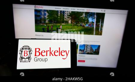 Persona che tiene il cellulare con il logo della società britannica The Berkeley Group Holdings plc sullo schermo di fronte al sito web. Mettere a fuoco sul display del telefono. Foto Stock