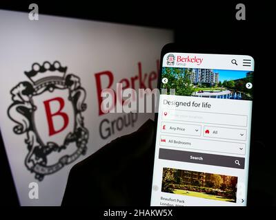 Persona che detiene il cellulare con sito web della società britannica The Berkeley Group Holdings plc su schermo con logo. Concentrarsi sul centro del display del telefono. Foto Stock