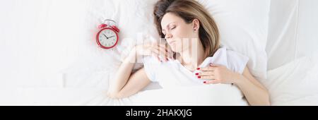 Giovane donna sdraiata a letto vicino alla sveglia rossa vista dall'alto Foto Stock