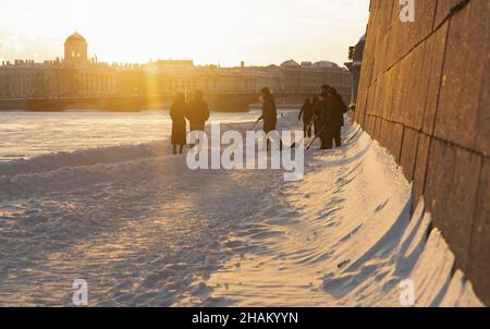 San Pietroburgo, Russia - 22 febbraio 2021: I cadetti con le pale rimuovono la neve vicino alle mura della fortezza di Pietro e Paolo e di una coppia ambulante Foto Stock