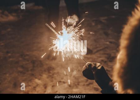 il ragazzo tiene un luccicante nelle sue mani mentre festeggia un nuovo anno per strada di notte. Fuochi d'artificio nelle mani dei bambini durante la celebrazione di Capodanno Foto Stock