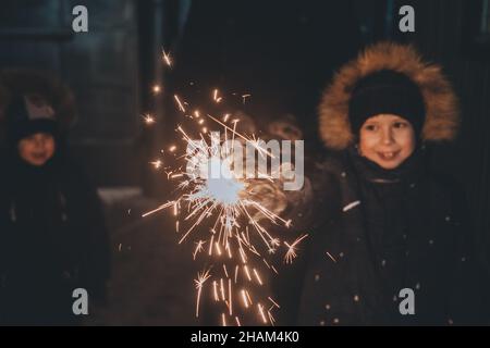 il ragazzo tiene un luccicante nelle sue mani mentre festeggia un nuovo anno per strada di notte. Fuochi d'artificio nelle mani dei bambini durante la celebrazione di Capodanno Foto Stock