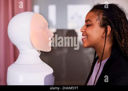 Giovane donna che guarda l'assistente vocale del robot Foto Stock